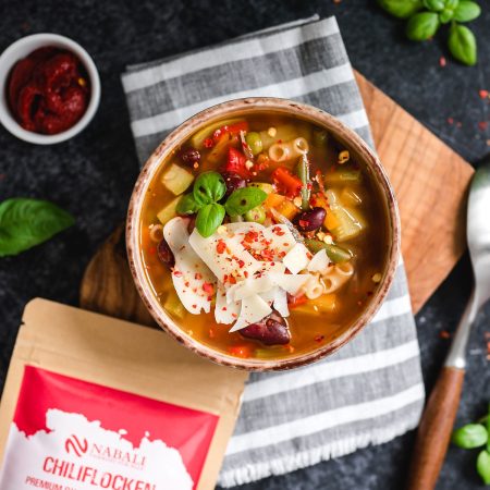 Eine schmackhafte Gemüsesuppe, garniert mit Chiliflocken und frischen Kräutern, serviert in einer rustikalen Schüssel auf einem Holzbrett.